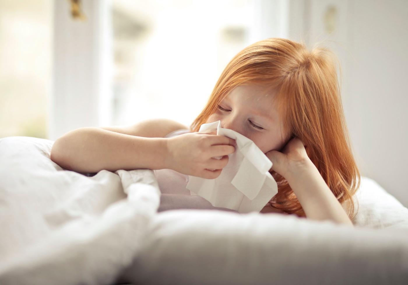 Criança constipada na cama a assoar o nariz
