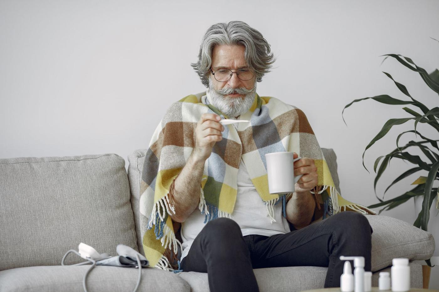 Homem mais velho sentado no sofá, com uma manta e uma caneca