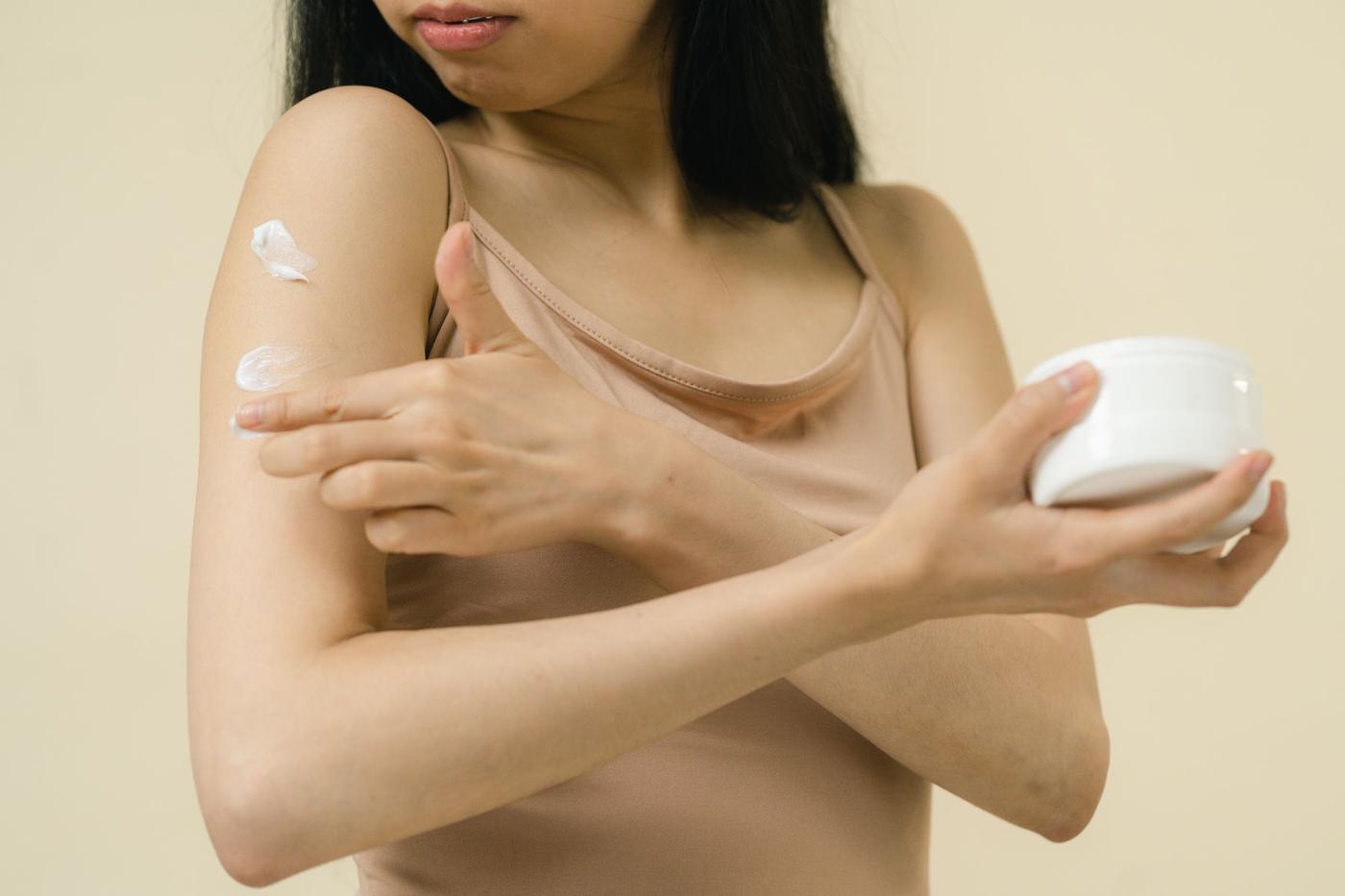 Mulher a aplicar creme hidratante no braço