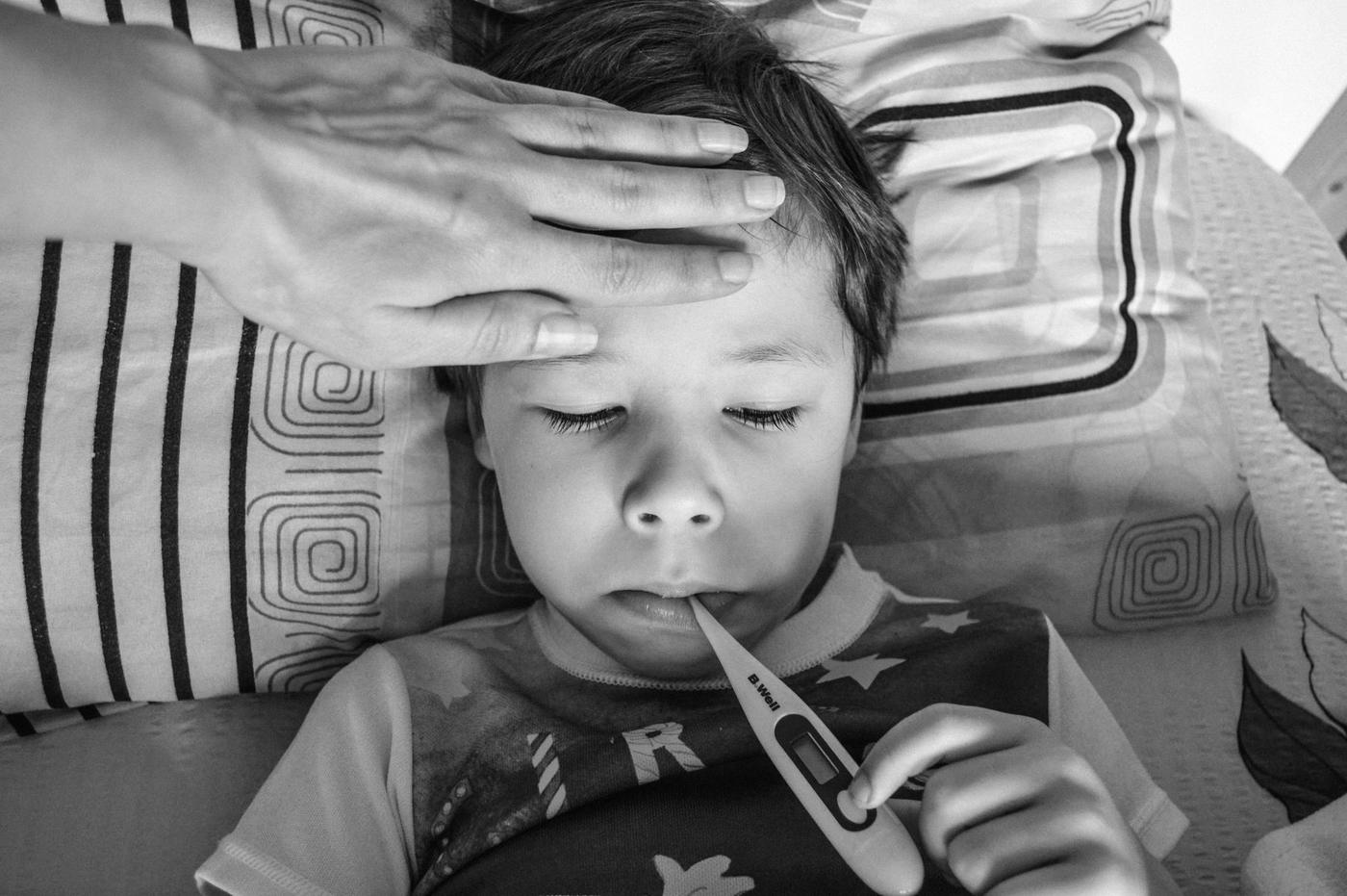 Criança na cama com termómetro e mão na testa